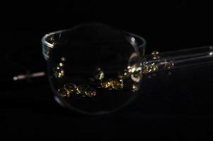 Visualizza attraverso ingrandimento bicchiere per traslucido gel capsule di d'oro colore contro il sfondo di petri piatto su nero foto