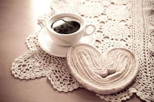 bianca tazza di nero caffè e un' dolce burroso biscotto su il tavolo foto