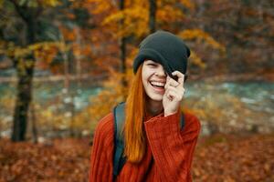 donna nel un' cappello e un' maglione con un' zaino su sua indietro divertimento autunno paesaggio fiume foto