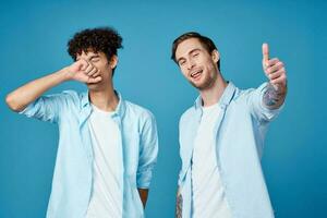 giovane ragazzi nel il stesso camicie e magliette siamo Esprimere a gesti con loro mani su un' blu sfondo amici foto