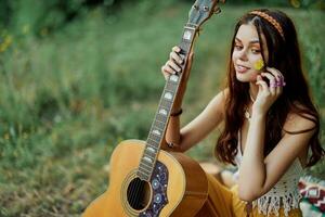 contento hippie donna con un' chitarra rilassante nel natura seduta su un' plaid sorridente e godendo il Visualizza. stile di vita nel armonia con natura e se stesso foto