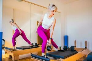 bionda donna è esercizio su pilates riformatore letto nel sua casa. foto