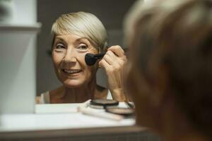 bellissimo maturo donna è l'applicazione trucco nel il bagno. foto