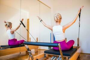 bionda donna è esercizio su pilates riformatore letto nel sua casa. foto