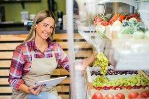 donna lavori nel frutta e verdure negozio. lei è Tenere un' grappolo di uva. foto