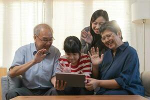 contento famiglia asiatico anziano nonno, nonna avere divertimento, sorridente genitore, ragazza utilizzando touchpad Guardando divertente video chiamata, giocare Giochi e prendere foto autoscatto godere fine settimana insieme nel vivente camera a casa