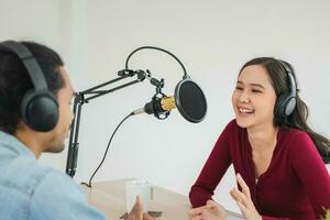 Sorridi Due asiatico giovane donna, uomo Radio padroni di casa nel cuffia, microfono mentre parlare, conversazione, registrazione Podcast nel emittente a studio insieme. tecnologia di fabbricazione disco Audio concetto. foto