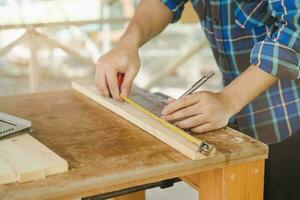 carpenteria professionale, mano di asiatico giovane uomo, maschio falegname uso nastro misurare, attrezzo su tavola legna nel piccolo negozio. lavorazione del legno, mobilia fabbricazione, costruzione industria. proprietario piccolo attività commerciale le persone. foto