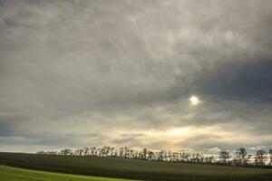 meraviglioso denso grigio nuvole con sole nel un' paesaggio con i campi foto