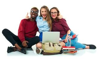 tre studenti seduta con libri, il computer portatile e borse isolato su bianca sfondo foto