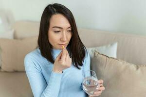 asiatico donna prende pillola con bicchiere di acqua nel mano. stressato femmina potabile sedato antidepressivo medicinali. donna si sente depresso, assunzione droghe. medicinali a opera foto