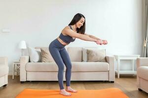 asiatico donna esercizio con manubri a casa. contento femmina fare braccio allenarsi utilizzando manubri foto