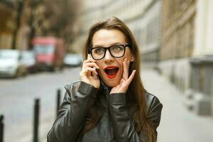 sorpreso donna d'affari a piedi giù il strada e parlando su inteligente Telefono foto