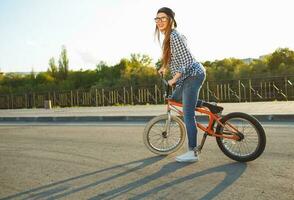 bello giovane donna nel un' cappello equitazione un' bicicletta su città sfondo nel il luce del sole all'aperto foto