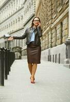 donna d'affari a piedi giù il strada mentre parlando su inteligente Telefono foto