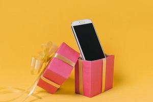cellulare con schermo vuoto e confezione regalo rosa su sfondo giallo foto