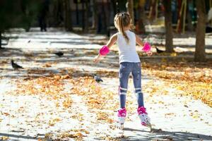 poco ragazza su rullo pattini e tram protezione equitazione nel il autunno parco. salutare stile di vita concetto. foto