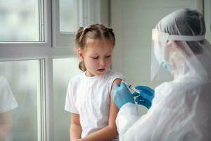 medico è mani nel gomma da cancellare guanti fa un' tiro nel il spalla di un' bambino nel un' medico maschera. vaccinazione contro coronavirus. covid-19 vaccino. il medico vaccina il bambino prende un' influenza sparo. foto