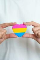 pansexual orgoglio giorno e lgbt orgoglio mese concetto. mano Tenere rosa, giallo e blu cuore forma per lesbica, gay, bisessuale, transgender, strano e pansexual Comunità foto