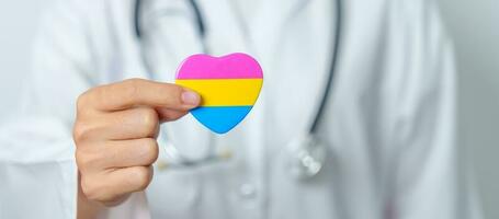 pansexual orgoglio giorno e lgbt orgoglio mese concetto. medico mano Tenere rosa, giallo e blu cuore forma per lesbica, gay, bisessuale, transgender, strano e pansexual Comunità foto