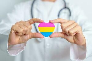 pansexual orgoglio giorno e lgbt orgoglio mese concetto. medico mano Tenere rosa, giallo e blu cuore forma per lesbica, gay, bisessuale, transgender, strano e pansexual Comunità foto