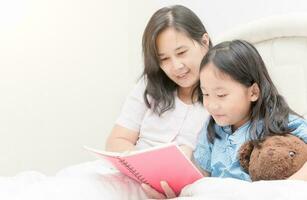 madre e figlia lettura libro su letto, foto