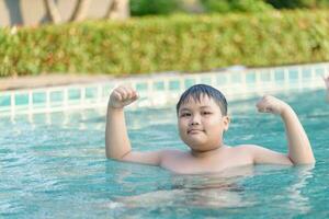 obeso Grasso ragazzo mostrare muscolo nel nuoto piscina foto