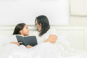 madre leggere libro con figlia insieme su letto foto