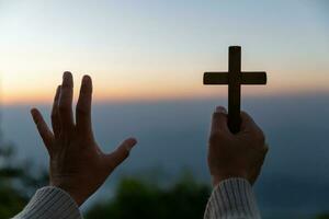 persona mani palma su preghiere e culto di attraversare con credenza nel Gesù Cristo. Eucaristia terapia Dio benedice aiuto, speranza, e fede, cristiano religione concetto su tramonto sfondo. foto