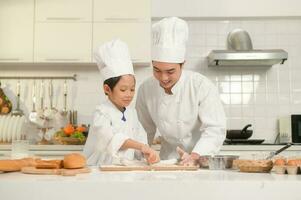 giovane asiatico padre e il suo figlio indossare capocuoco uniforme cottura al forno insieme nel cucina a casa foto