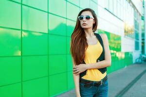 elegante alla moda donna nel occhiali da sole in piedi vicino un' verde costruzione. foto