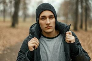 bello alla moda uomo nel un' nero a maglia cappello con un' inverno giacca in posa nel autunno parco. foto