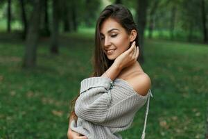 bellissimo contento giovane donna sorridente nel un' grigio maglione nel un' verde parco. foto