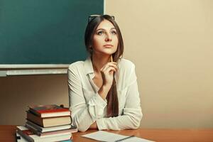 bellissimo giovane donna seduta a il tavolo con libri e pensiero. indietro per scuola. foto