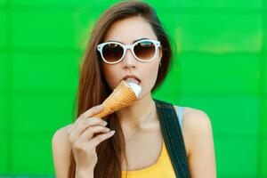 giovane bellissimo donna nel occhiali da sole mangiare ghiaccio crema su un' verde sfondo. foto