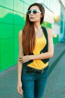 elegante giovane ragazza nel occhiali da sole e un' giallo camicia su un' verde sfondo. foto