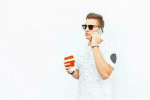 elegante giovane uomo Tenere un' tazza di caffè nel mano e parlando su il Telefono. foto