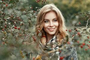 bellissimo giovane ragazza con un' Sorridi nel un' caldo sciarpa vicino un' albero con frutti di bosco foto