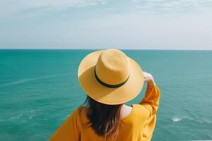 indietro Visualizza di un' donna indossare un' cappello seduta su un' spiaggia. ai generato foto
