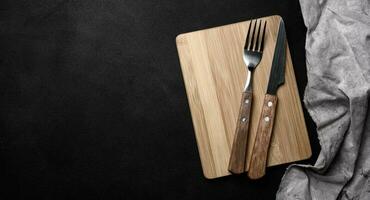 forchetta e coltello con di legno maniglia e taglio tavola su nero sfondo, superiore Visualizza foto