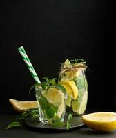 limonata nel un' trasparente bicchiere con Limone, lime, rosmarino rametti e menta le foglie su un' nero sfondo foto