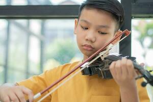 un ragazzino asiatico che suona e pratica lo strumento a corda musicale del violino contro in casa, concetto di educazione musicale, ispirazione, studente di scuola d'arte per adolescenti. foto