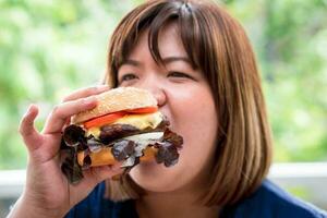 Affamato sovrappeso donna Tenere Hamburger su di legno piatto dopo consegna uomo consegna Alimenti a casa. concetto di abbuffata mangiare disturbo letto e rilassante con mangiare Rifiuto cibo. foto