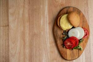 superiore Visualizza di fresco gustoso fatti in casa Hamburger con fresco la verdura, lattuga, pomodoro, formaggio accanto affettato pomodori su un' taglio tavola. gratuito spazio per testo foto