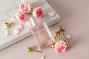 un elegante bicchiere bottiglia di Da donna profumo o eau de Toilette con un' delicato rosa profumo Appoggiato su un' marmo bianca podio con piccolo vivere Rose. foto