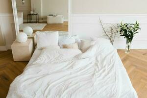 un' Doppio letto con bianca biancheria e beige cuscini nel un' luminosa scandinavo Camera da letto, un' letto su il pavimento e fiori nel un' vaso foto