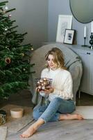 bella giovane donna nel un' accogliente maglione e jeans decora un' Natale albero con palloncini a partire dal un' cestino a casa foto