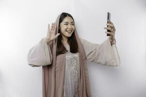 un' contento asiatico musulmano donna indossare un' foulard, felicemente parlando durante video chiamata, isolato di bianca sfondo foto