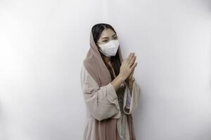 ritratto di un' giovane bellissimo asiatico musulmano donna indossare un' maschera e foulard Esprimere a gesti eid mubarak saluto durante pandemia foto