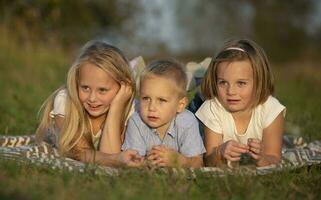 sorelle e poco fratello menzogna su il erba. bambini giocare nel il prato. un' contento famiglia. foto